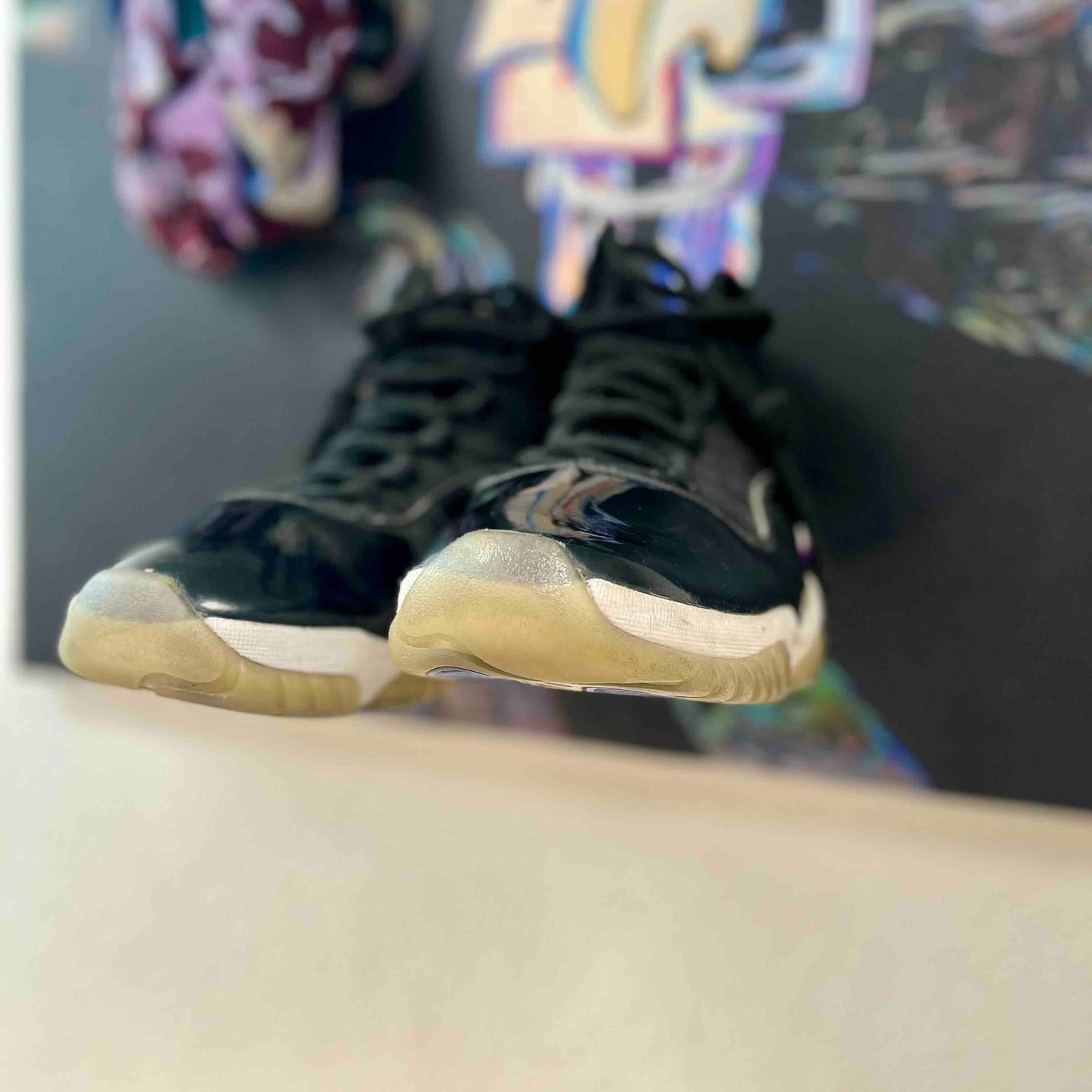 Black high-top sneakers with white soles on a reflective surface, with colorful abstract art in the background.